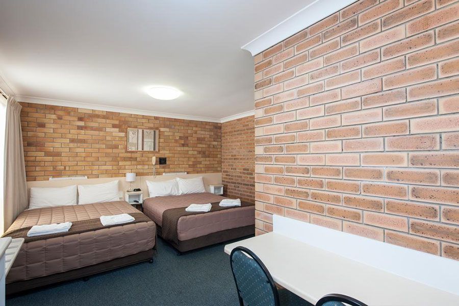 A room with light brown brick wall, two brown queen beds