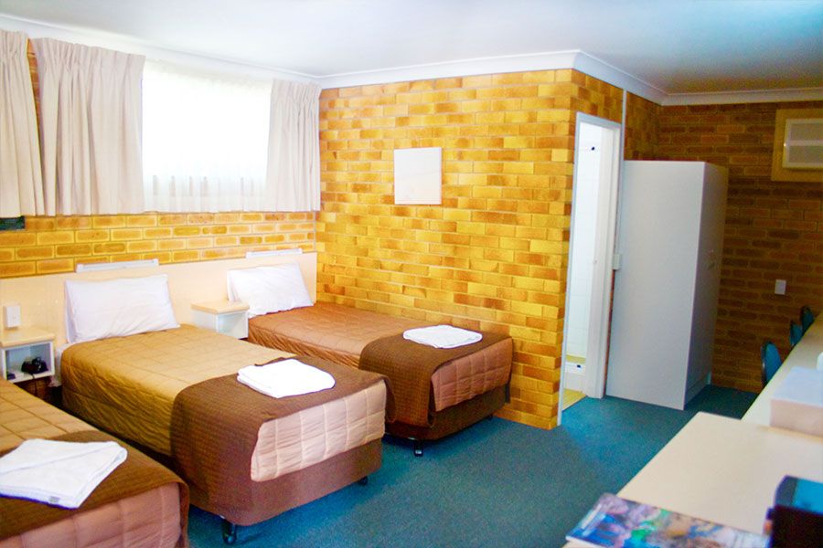 A room with one brown queen bed and two brown single beds, bathroom door opened