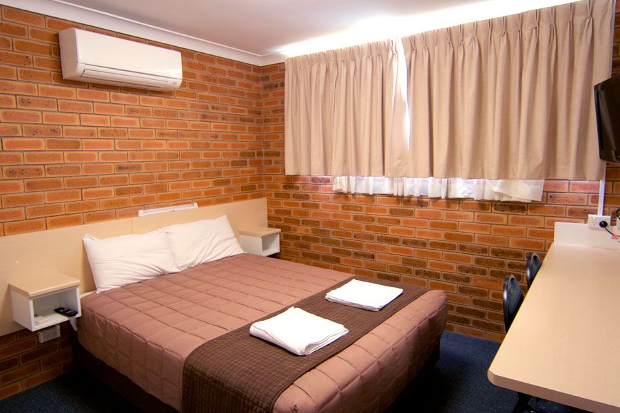 A room with brown queen bed, an air conditioner and curtains