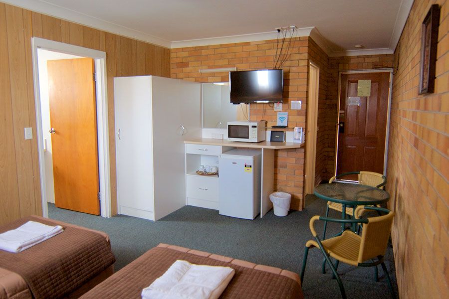 A room with beds, desk set-up, microwave oven, closets and TV set