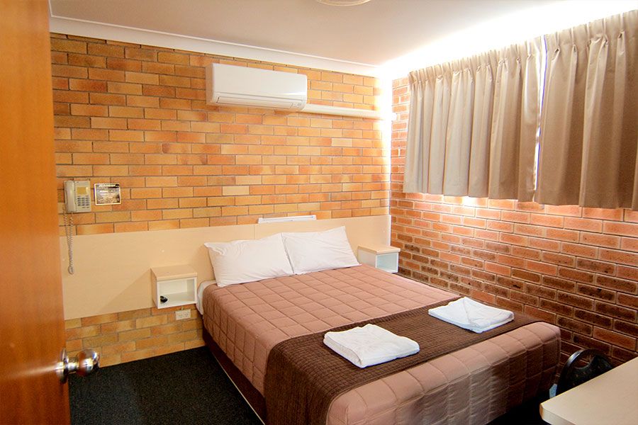 A bedroom with brown brick walls, that has one queen bed